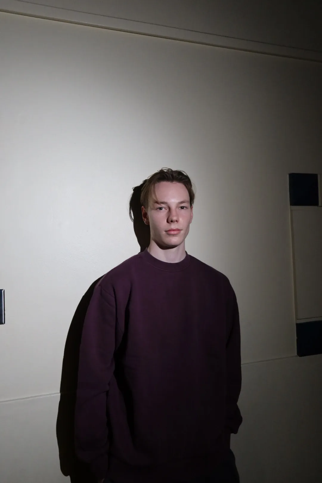 Blank burgundy crewneck sweatshirt worn front-facing against a white wall