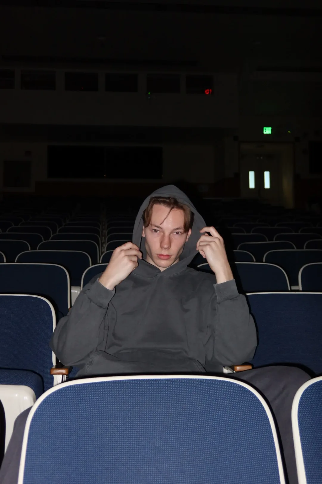 Model pulling up the hood of a blank grey hoodie in a lecture hall