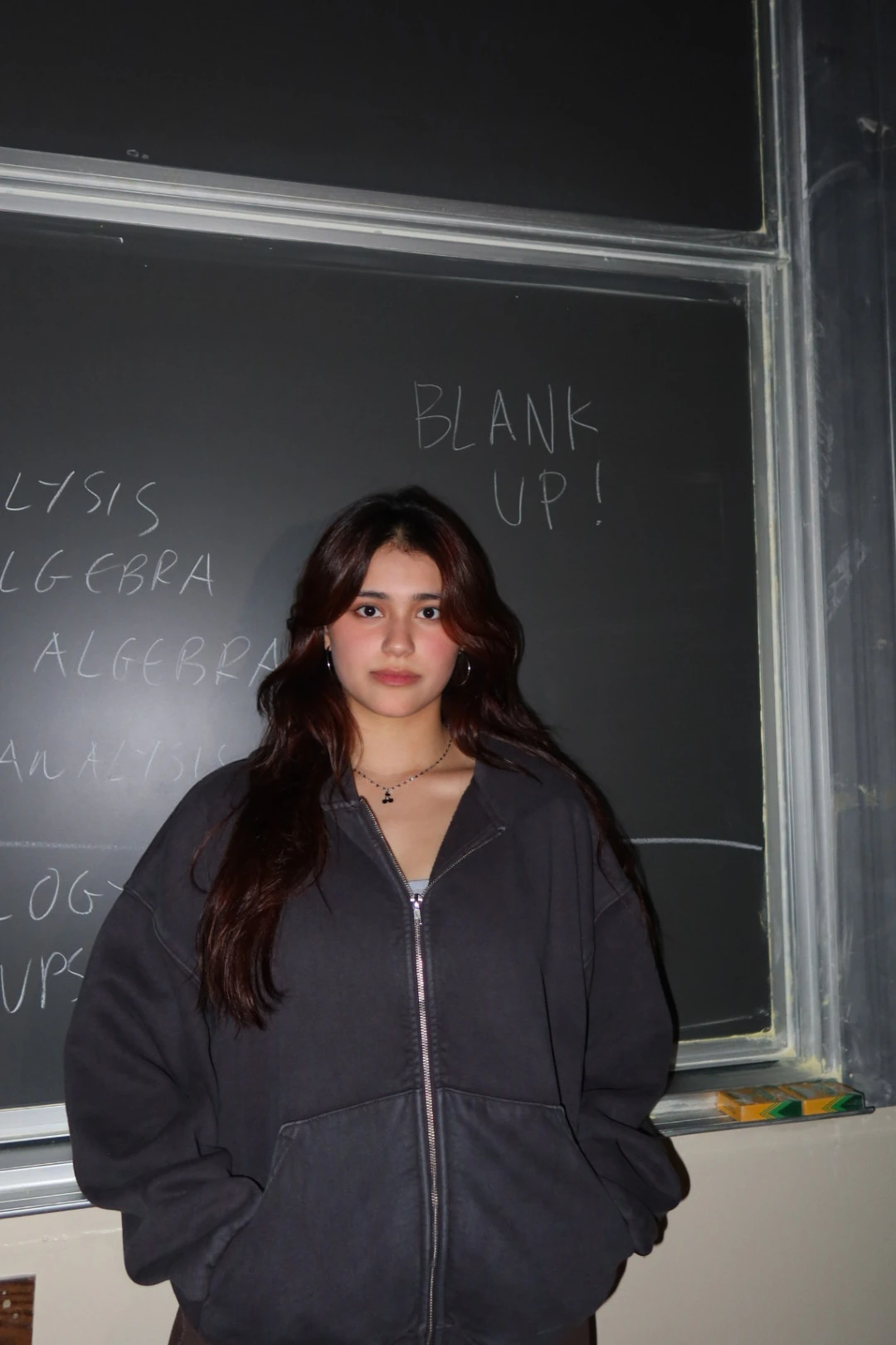 Student in a blank charcoal zip hoodie in front of a chalkboard reading blankup