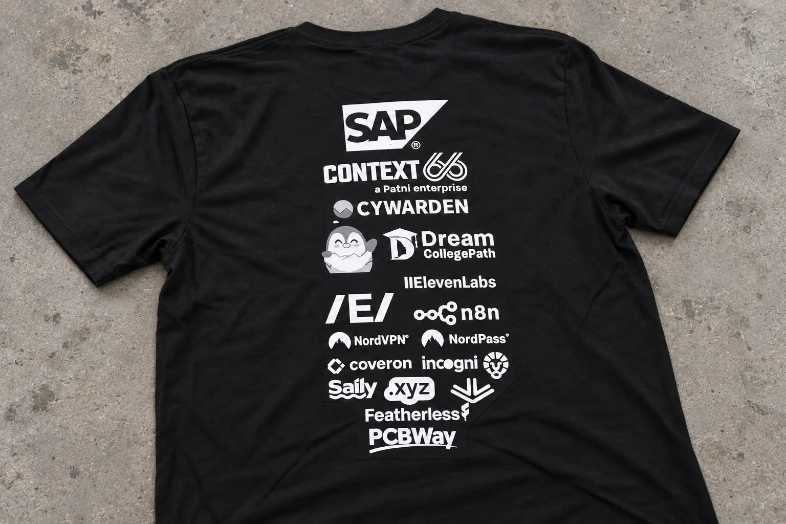 AI-generated back detail of a black dublinhacx crewneck tee on a continuous gray worn concrete floor under neutral indoor light, with a tall white sponsor stack and natural contact shadows