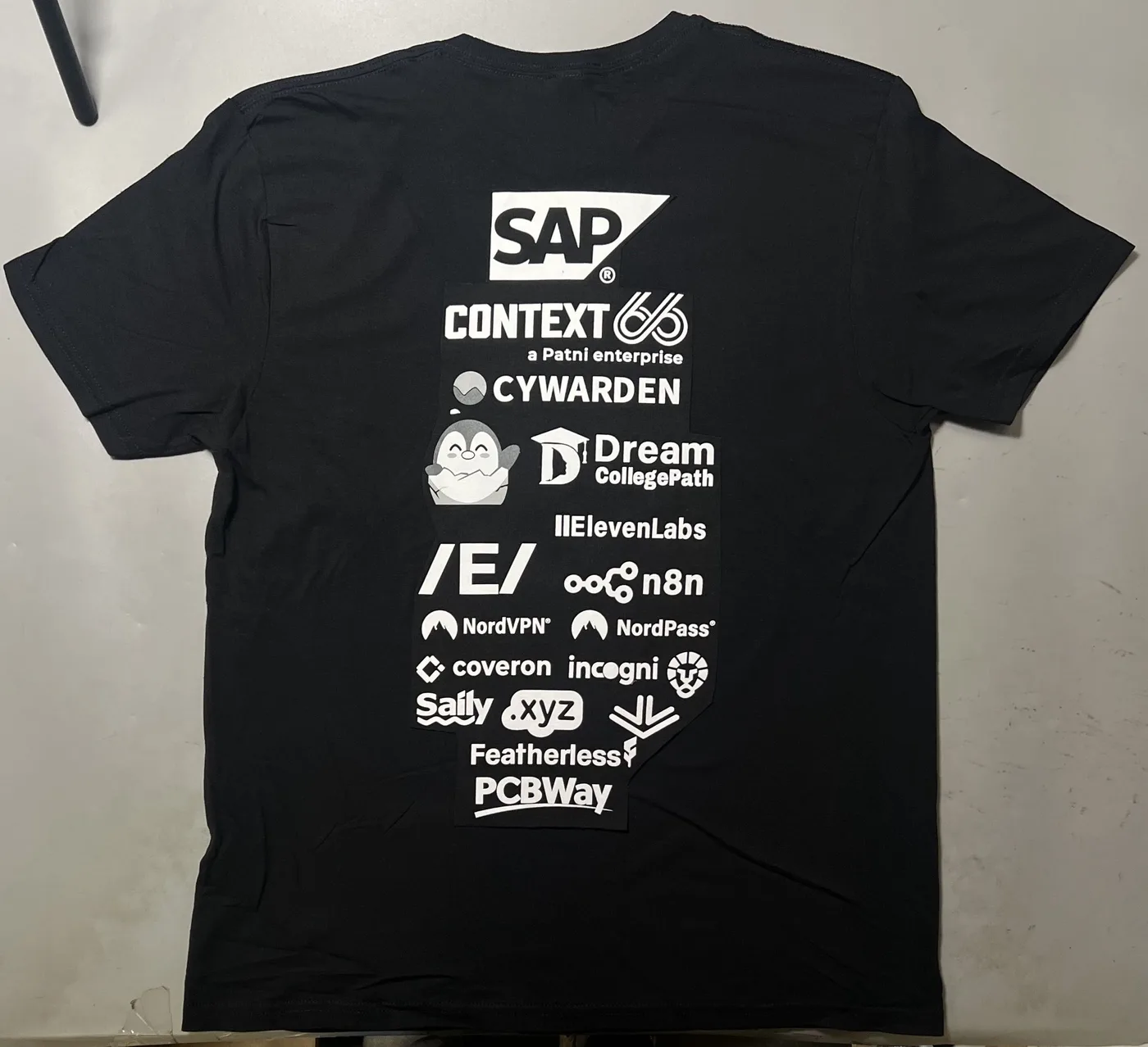 Supplied source photo of the back of a black dublinhacx crewneck tee with a tall white sponsor stack