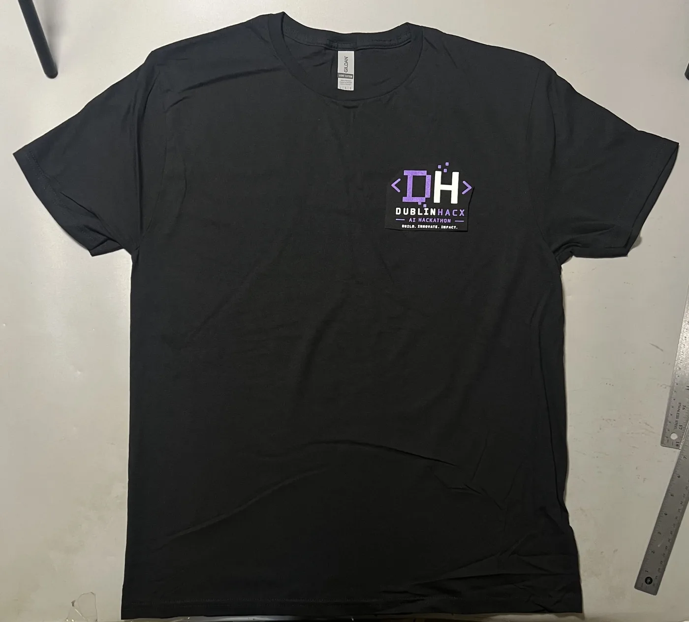 Supplied source photo of the front of a black dublinhacx crewneck tee with a small purple-and-white DH coding logo on the left chest