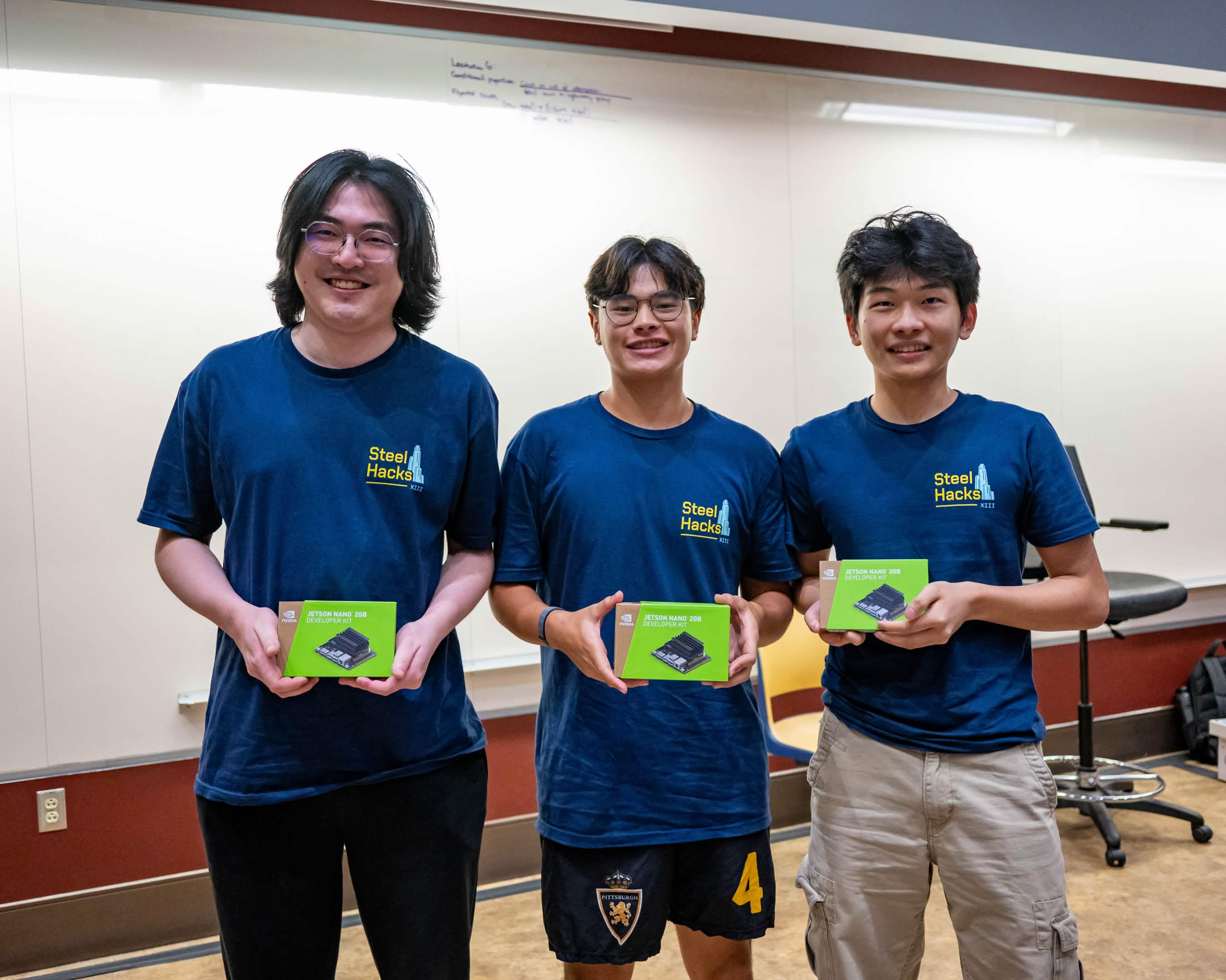 Three SteelHacks participants wearing navy event shirts and holding prizes